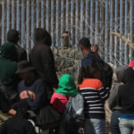 Migrantes esperan entre alambres de púas mientras un agente estadounidense vigila, en Ciudad Juárez, Chihuahua. Foto de EFE/ Luis Torres
