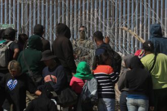 Migrantes esperan entre alambres de púas mientras un agente estadounidense vigila, en Ciudad Juárez, Chihuahua. Foto de EFE/ Luis Torres