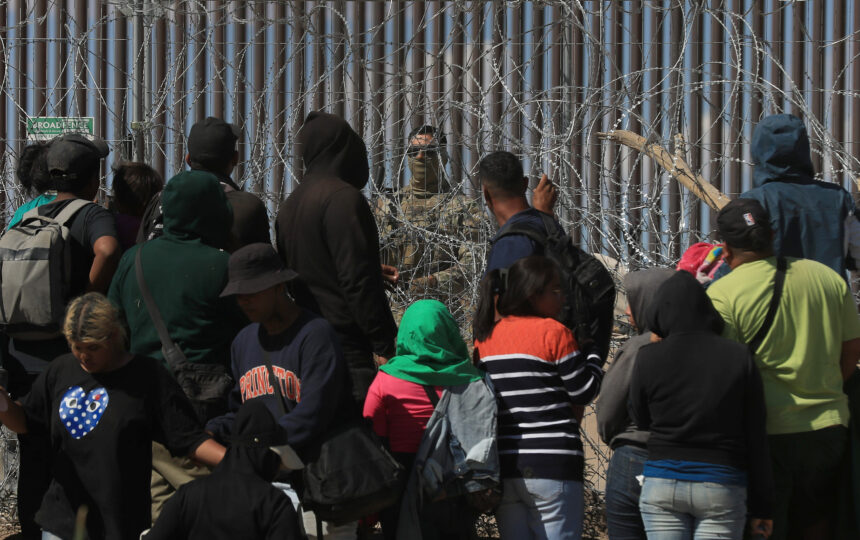 Migrantes esperan entre alambres de púas mientras un agente estadounidense vigila, en Ciudad Juárez, Chihuahua. Foto de EFE/ Luis Torres