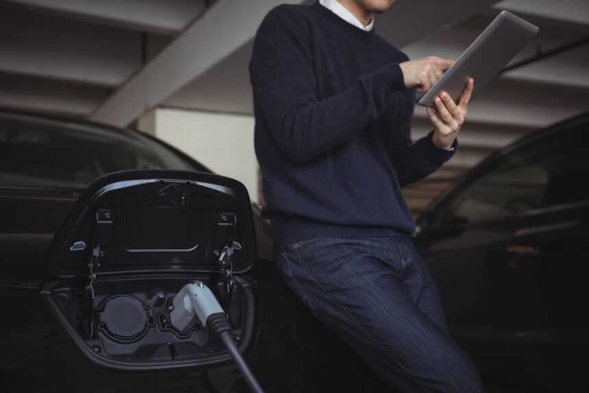 man using digital tablet while charging electric car 1