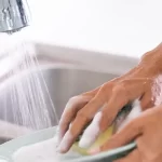 Persona lavando trastes con el agua desperdiciándose