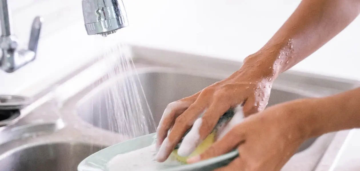 Persona lavando trastes con el agua desperdiciándose